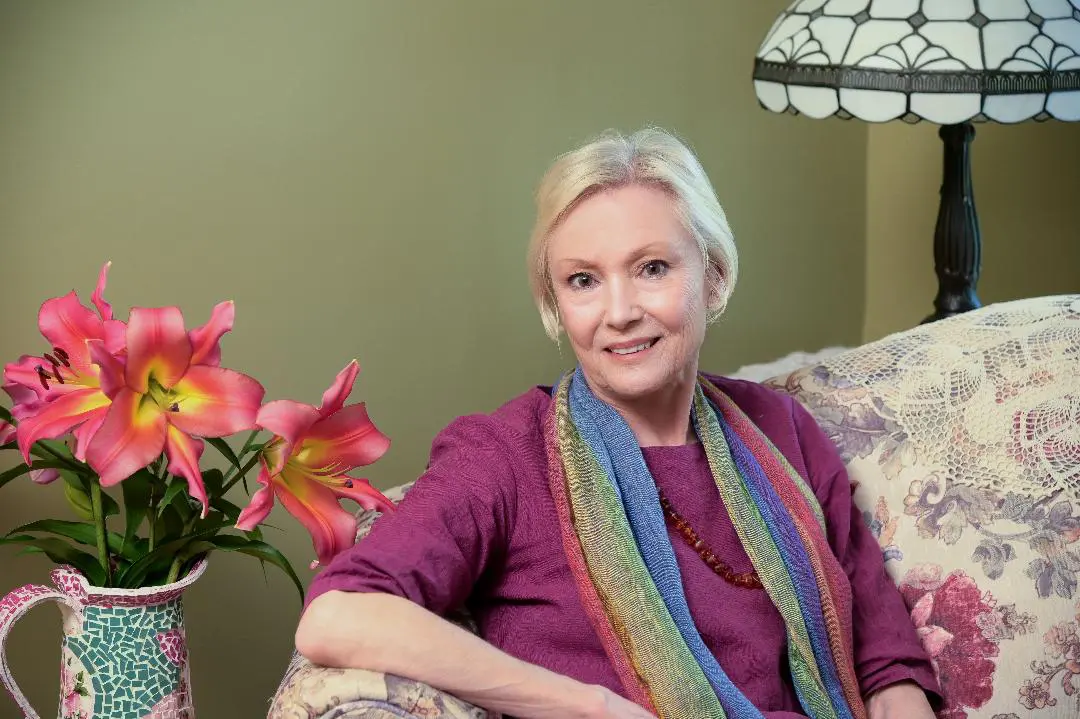 A woman sitting on top of a couch in front of flowers.